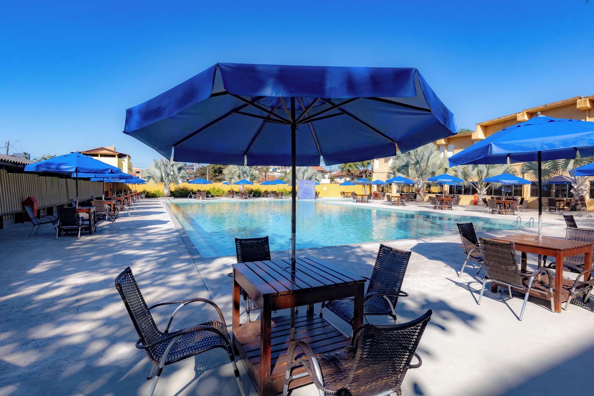 Área de piscina com espreguiçadeiras, guarda-sóis e céu azul.