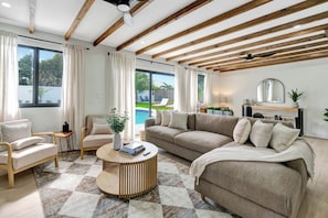 A modern living room with a sofa, armchairs, a coffee table, and a view of a pool. - Tiki on the Green - Pool, Bar, and Putting Green (Palm Beach Gardens)