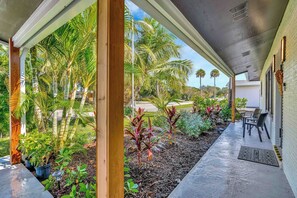 A covered outdoor area with a concrete floor, wooden pillars, and various plants including palm trees and shrubs. - Tiki on the Green - Pool, Bar, and Putting Green (Palm Beach Gardens)