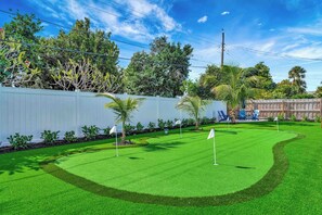 A well-maintained golf course with a white fence, palm trees, and a clear sky. - Tiki on the Green - Pool, Bar, and Putting Green (Palm Beach Gardens)