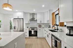 A modern kitchen with white cabinetry, stainless steel appliances, and a central island. - Tiki on the Green - Pool, Bar, and Putting Green (Palm Beach Gardens)