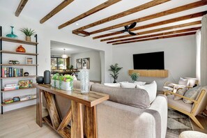 A modern living room with a wooden ceiling, a sofa, a coffee table, and a bookshelf. - Tiki on the Green - Pool, Bar, and Putting Green (Palm Beach Gardens)