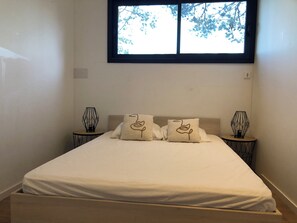 Ein Schlafzimmer mit einem Bett, zwei Nachttischen mit Lampen und einem Fenster mit Blick auf Bäume.