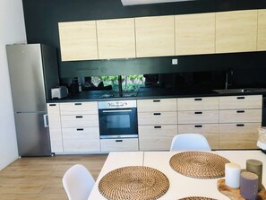 Eine moderne Küche mit Edelstahlkühlschrank, Holzschränken, integriertem Backofen und einem Essbereich mit weißem Tisch und Stühlen.