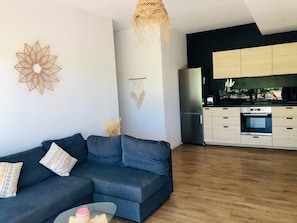 Un salon moderne avec un canapé gris foncé, une table basse en verre et des éléments décoratifs suspendus au mur.