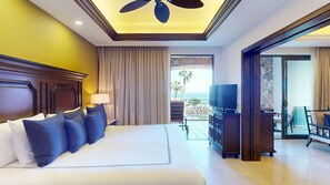 Ein Hotelzimmer mit einem großen Bett, einem Fernseher, einem Balkon mit Meerblick und einem Deckenventilator.