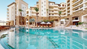 Ein Hotel mit Schwimmbad, Liegestühlen und einer Stein-Fassade.
