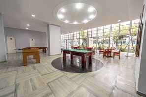 A billiards room with multiple tables and chairs, large windows, and a circular ceiling light. - Apt for 5 w/ AC 150m from Pitangueiras Beach (Guarujá)