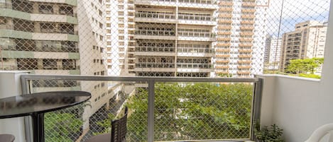 A balcony with a table and chairs, overlooking a cityscape with high-rise buildings.