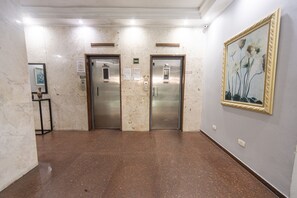 A corridor with two elevators, marble walls, and a framed artwork on the right. - Apt for 5 w/ AC 150m from Pitangueiras Beach (Guarujá)