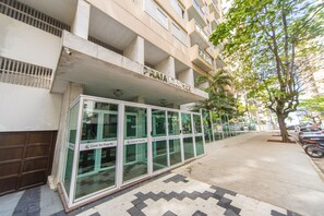 Um edifício com fachada de vidro, um letreiro com a inscrição 'Praia Mar 144' e uma área de entrada com piso de azulejos.