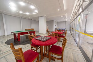 Quarto com mesa de bilhar, mesa de xadrez e várias cadeiras com almofadas vermelhas.