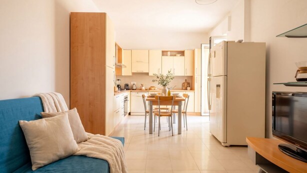 A modern living room with a sofa, a dining area with a table and chairs, a kitchen with cabinets and appliances, and a television on a stand. - Mediterra Spacious Apartment | Stylish 3BR in Bari (Bari)