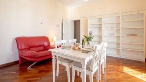A dining area with a white table and chairs, a red sofa, and a white shelving unit against the wall. - Mediterra Spacious Apartment | Stylish 3BR in Bari (Bari)