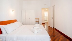 A hotel room with a bed, a wooden headboard, a nightstand, a wardrobe, and a bathroom visible through an open door. - Mediterra Spacious Apartment | Stylish 3BR in Bari (Bari)
