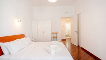 Una camera d'hotel con un letto, una testiera in legno, un comodino, un armadio e un bagno visibile attraverso una porta aperta.