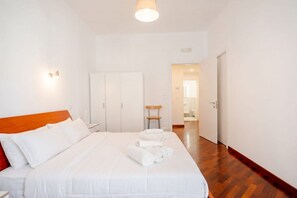 Una camera d'hotel con un letto, una testiera in legno, un comodino, un armadio e un bagno visibile attraverso una porta aperta.