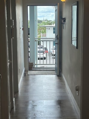 A hallway leading to a balcony with a view of parked cars and a building in the background. - Beautiful 1 bedroom condominium steps away from the sugar white beach! (Fort Walton Beach)