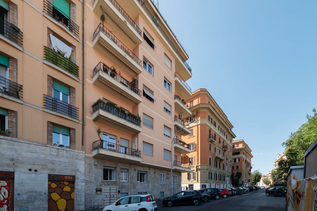 Un immeuble résidentiel à plusieurs étages, doté de balcons, avec des voitures garées et un ciel dégagé.