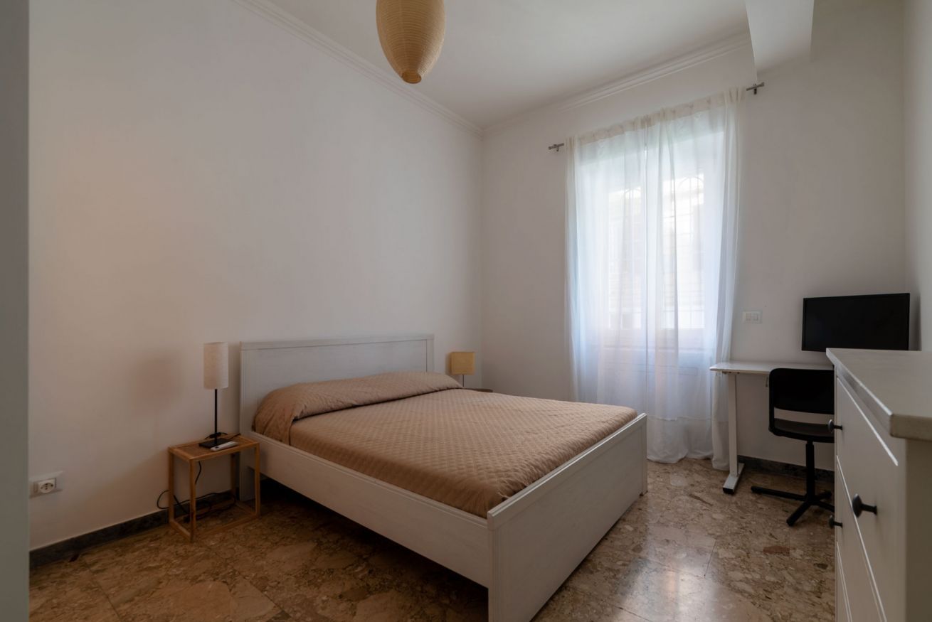 Quarto com cama, escrivaninha, cadeira e televisão.