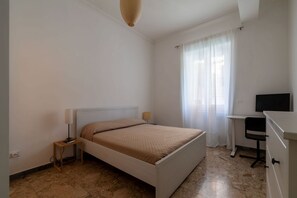 Quarto com cama, escrivaninha, cadeira e televisão.