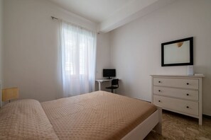 Ein Schlafzimmer mit Bett, Schreibtisch, Stuhl, Kommode und einem gerahmten Bild an der Wand.