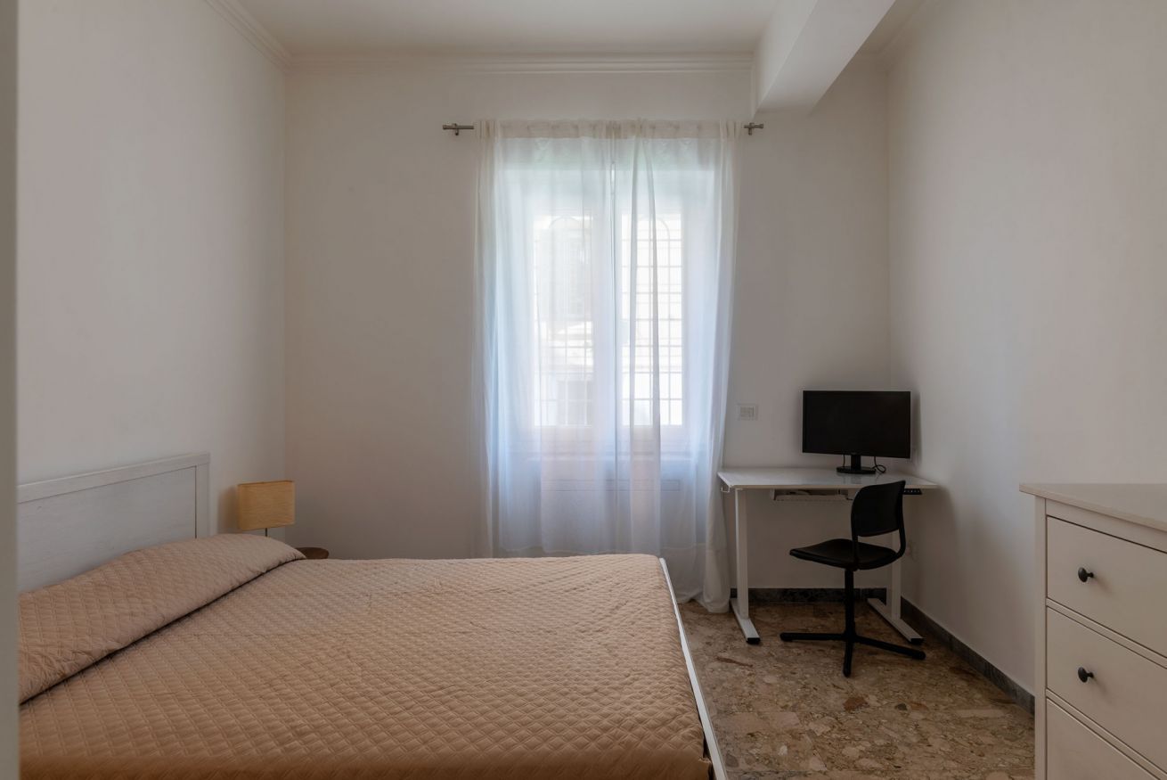 A bedroom with a bed, a desk with a chair, a television, and a wardrobe.