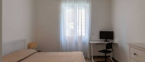A bedroom with a bed, a desk with a chair, a television, and a wardrobe.
