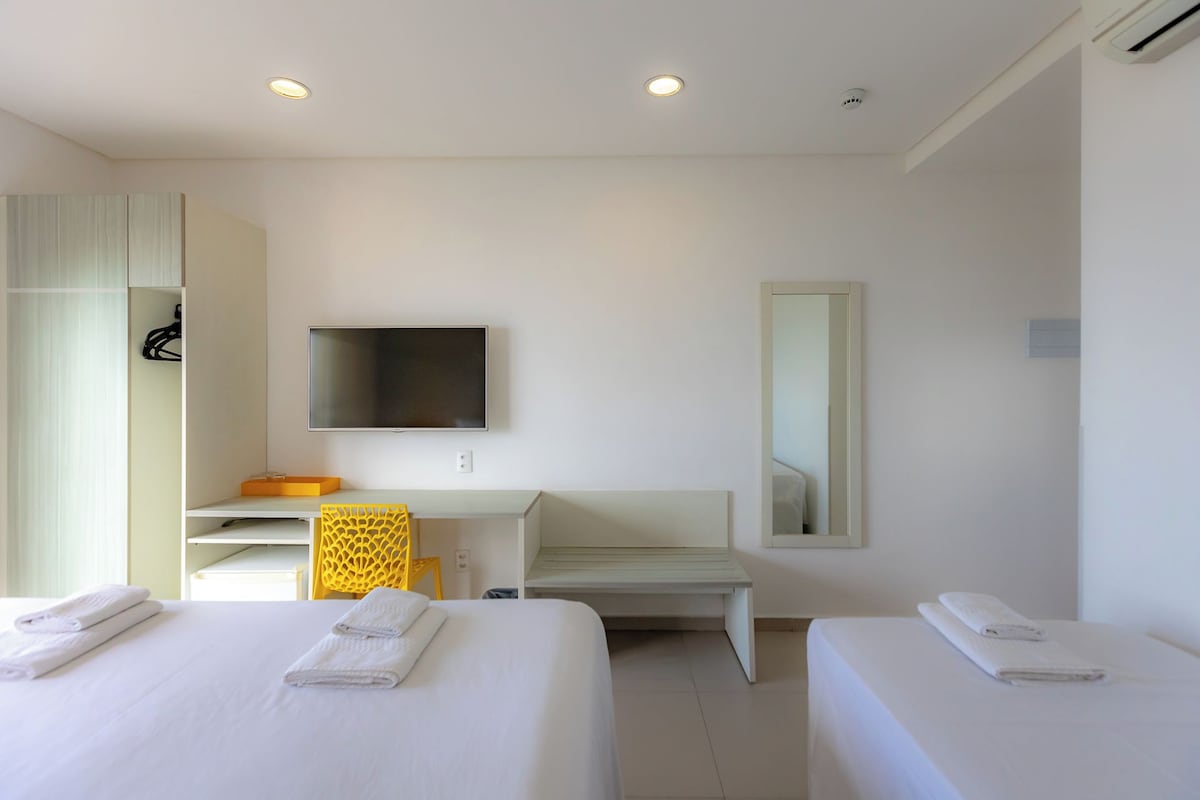A hotel room with two beds, a desk, a chair, a TV, and a mirror.