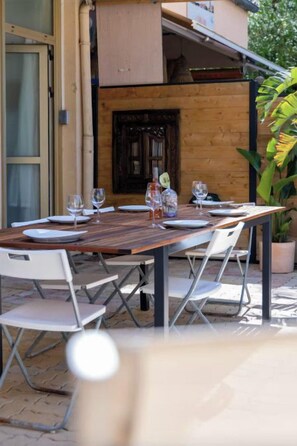 An outdoor dining area with a wooden table and chairs, a potted plant, and a wooden door in the background. - Apartment, big terrace, pool, walk to sea (Sanary-sur-Mer)