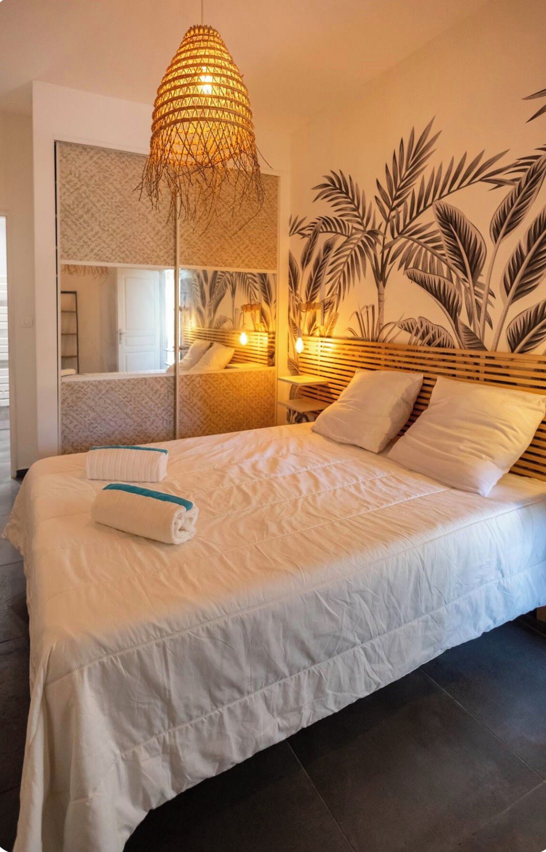 A hotel room with a bed, a large mirror, a wall mural, and a hanging light fixture.