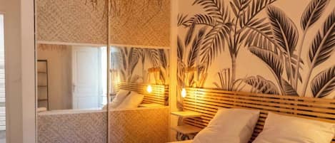 A hotel room with a bed, a large mirror, a wall mural, and a hanging light fixture.