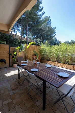 An outdoor patio with a wooden table set for dining, surrounded by potted plants and a wooden fence. - Apartment, big terrace, pool, walk to sea (Sanary-sur-Mer)