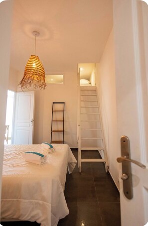 A bedroom with a bed, a hanging light fixture, a ladder, and a door leading to a staircase. - Apartment, big terrace, pool, walk to sea (Sanary-sur-Mer)