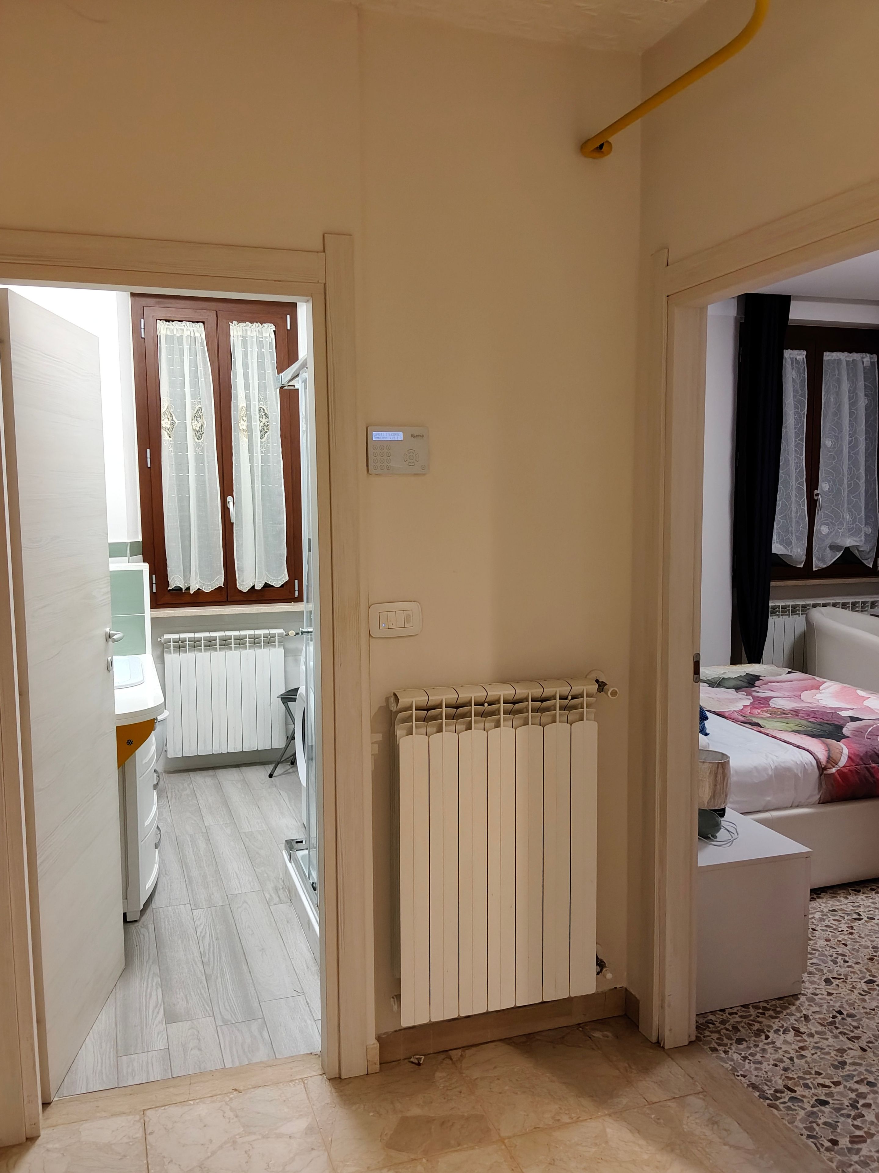 Ein Hotelzimmer mit Heizkörper, einem Bett mit floralem Überwurf und einem Badezimmer mit Toilette und Spiegel.