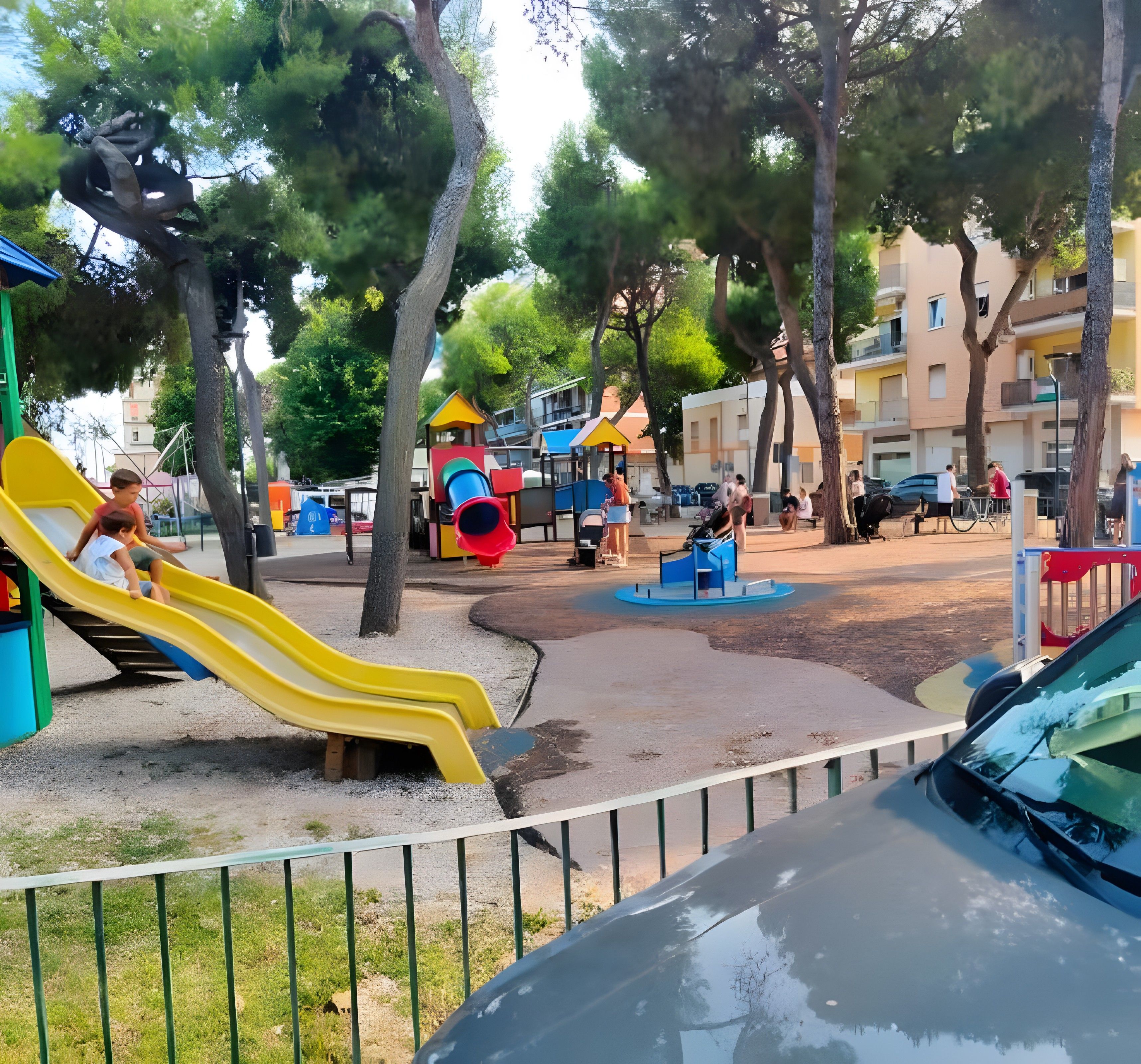 Ein Spielplatz mit Rutschen und Spielgeräten, umgeben von Bäumen und Gebäuden.