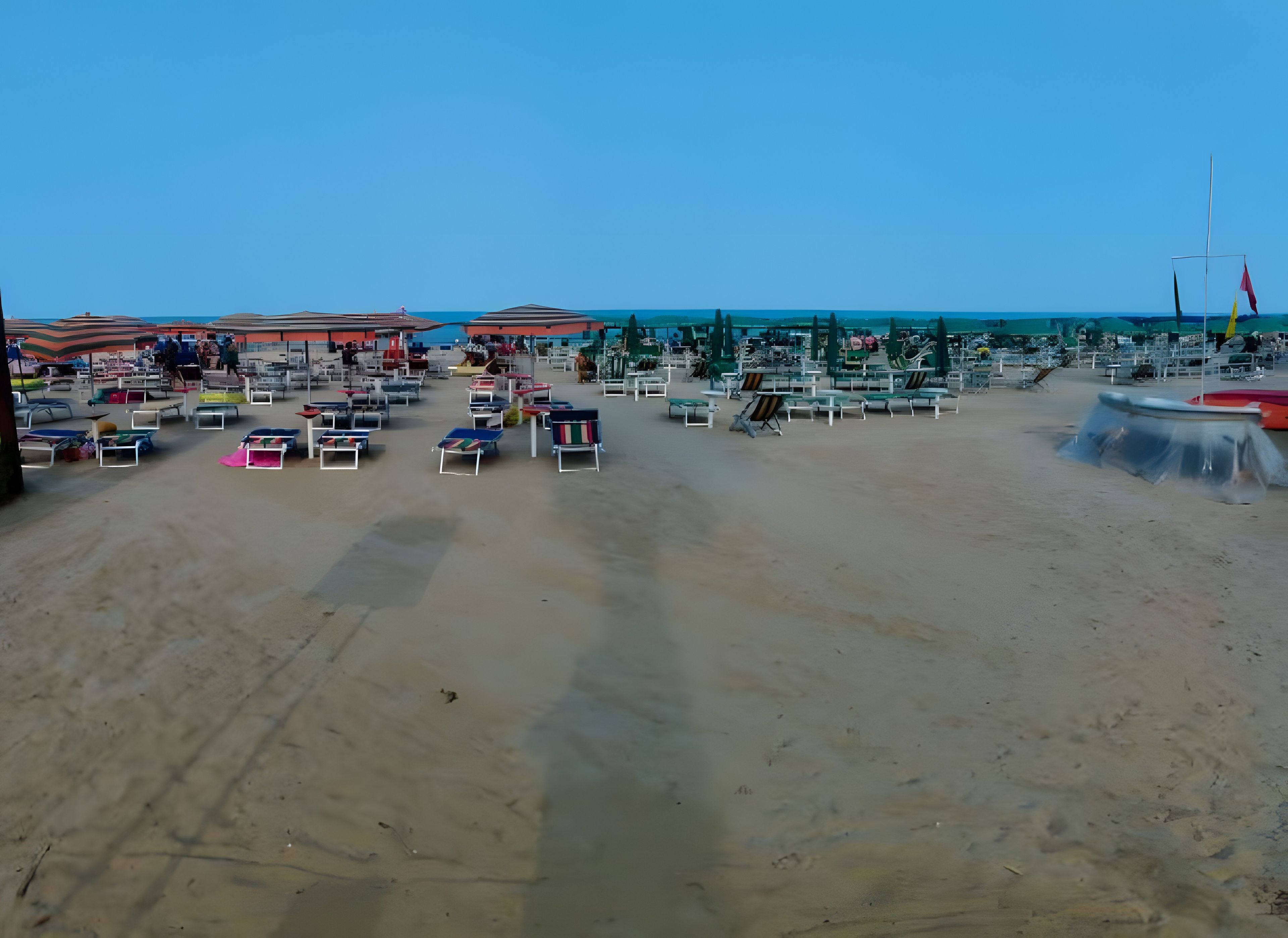 Una spiaggia con numerosi lettini e ombrelloni, cielo sereno e mare calmo.
