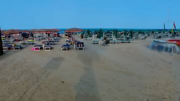 Una spiaggia con numerosi lettini e ombrelloni, cielo sereno e mare calmo.