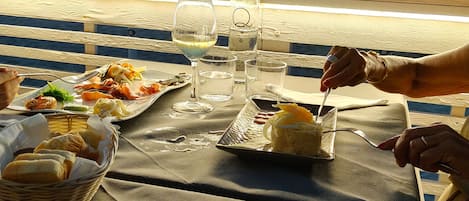 Una mesa con comida y bebidas en una playa, con sombrillas al fondo.