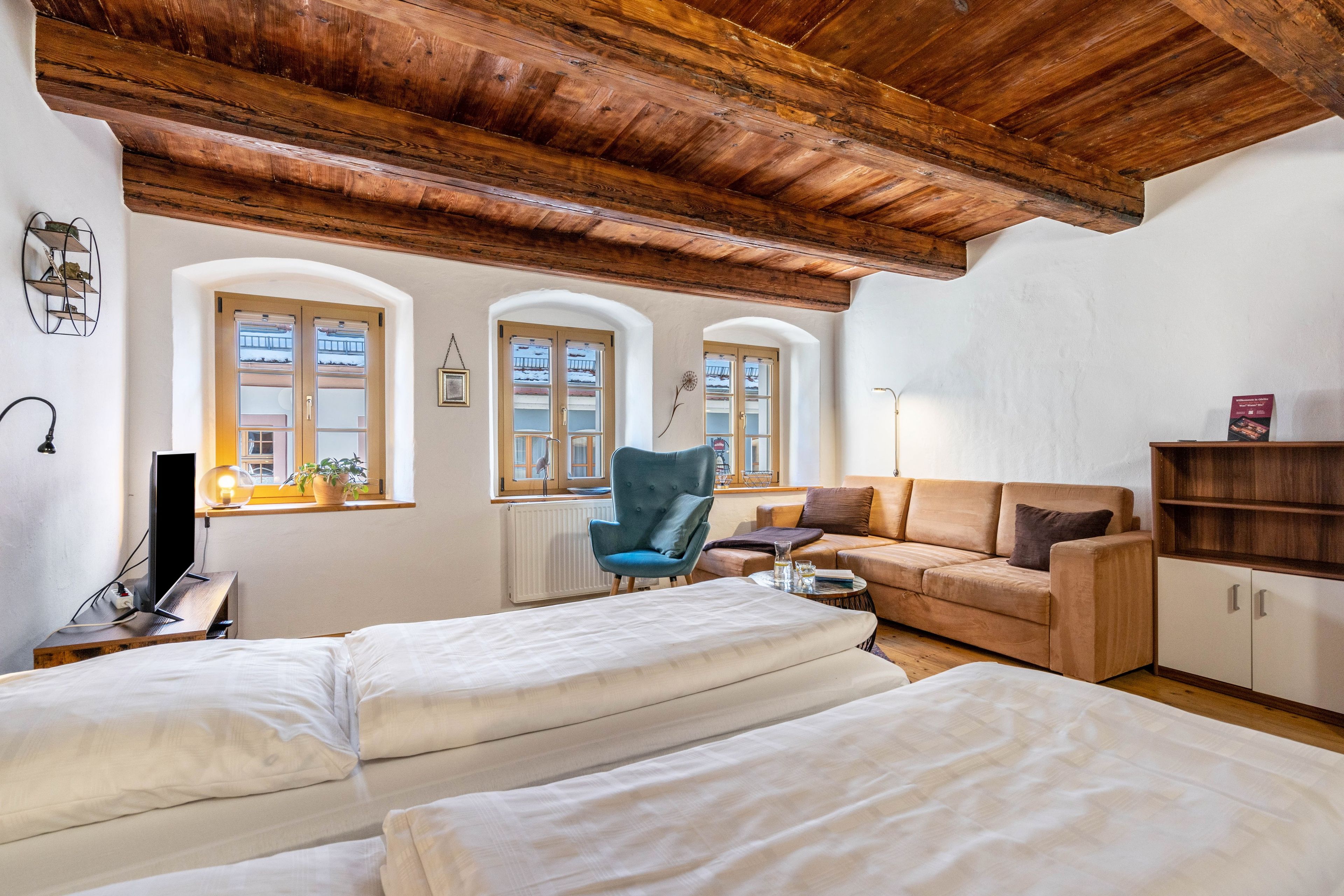 Ein Zimmer mit Holzboden, zwei Betten, einer Couch, einem Sessel und einer Heizung.