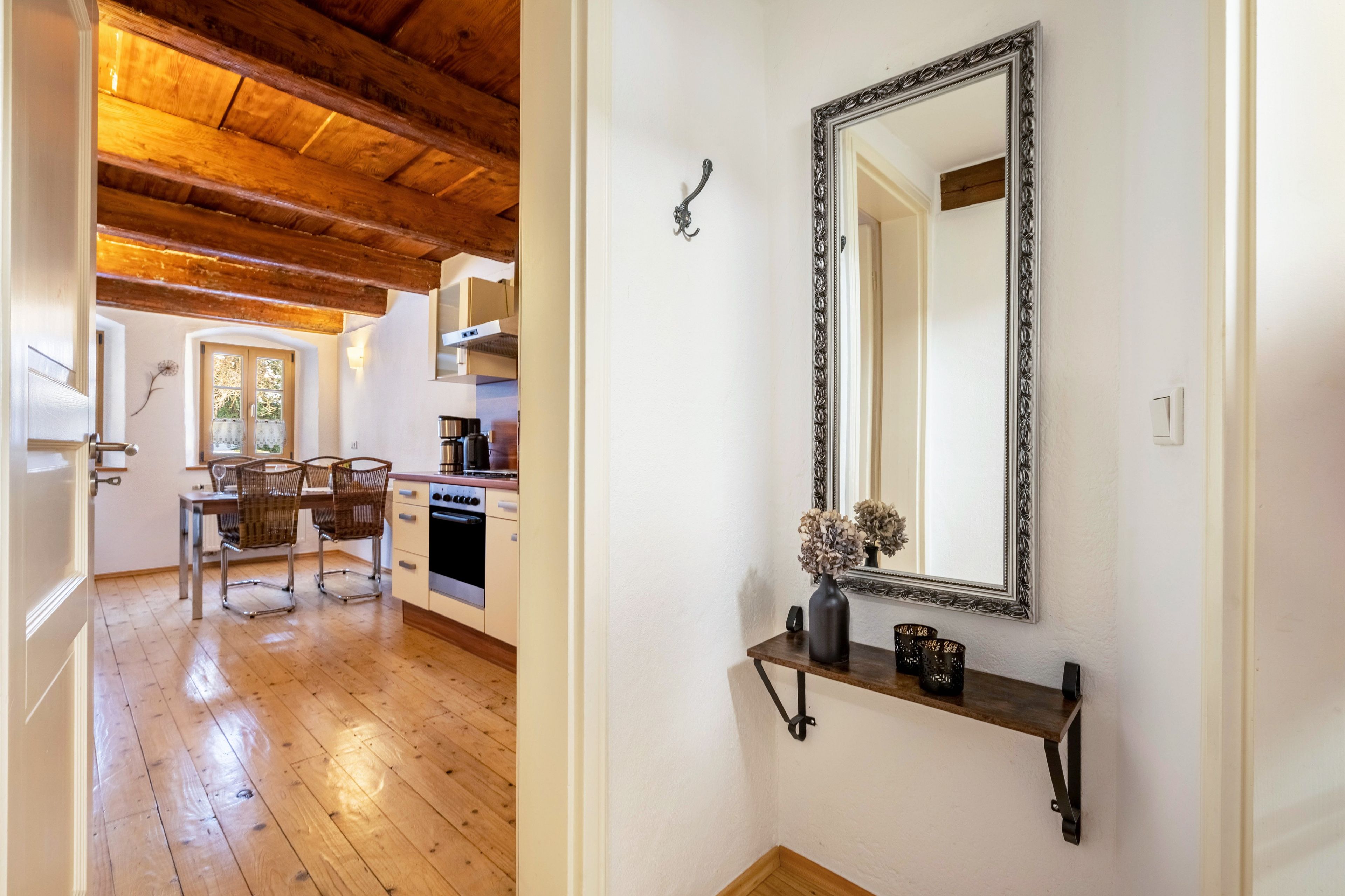 Una cucina moderna con pavimento in legno, un'area pranzo con sedie e un grande specchio a parete.