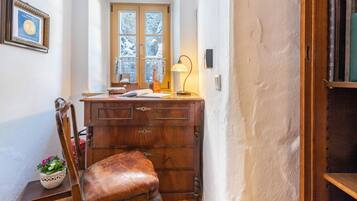Quarto de canto com escrivaninha de madeira, uma cadeira, janela com vista para árvores cobertas de neve e um certificado emoldurado na parede.