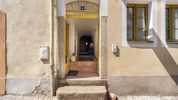 A building entrance with a yellow door, a tiled pathway leading to the entrance, and a window with yellow shutters.