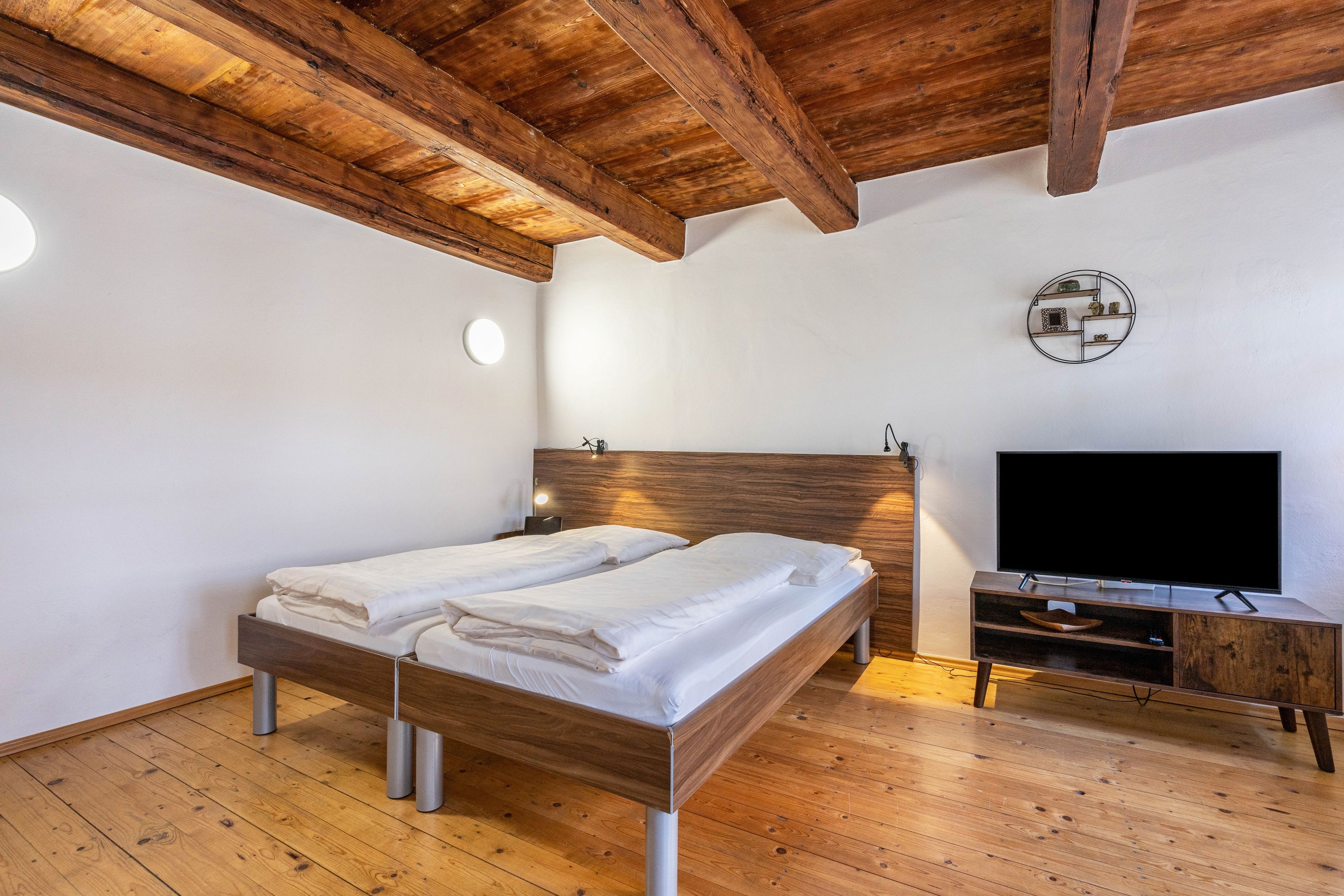 Quarto com cama de madeira, televisão e prateleira na parede.