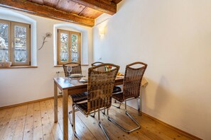 Un comedor con mesa de madera y cuatro sillas de mimbre, una ventana con vista a árboles nevados y techo de madera.