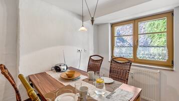 A dining area with a wooden table, chairs, a radio, and a window with a view of greenery.
