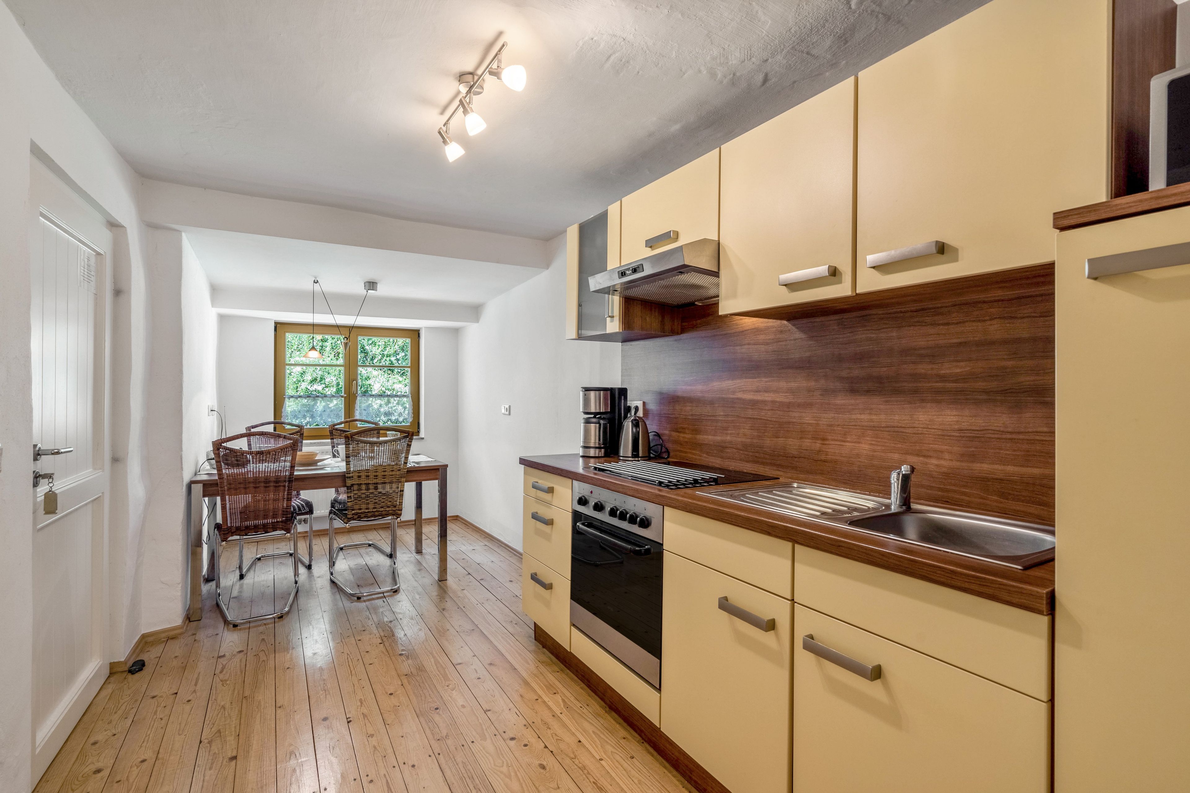 A kitchen with wooden flooring, a dining area with a table and chairs, and a window with a view of greenery.