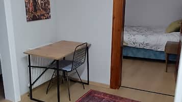 A room with a bed, a desk with a chair, a patterned rug, and a painting on the wall.
