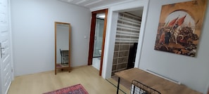 Quarto com porta de madeira, espelho, parede revestida de azulejos e um quadro.