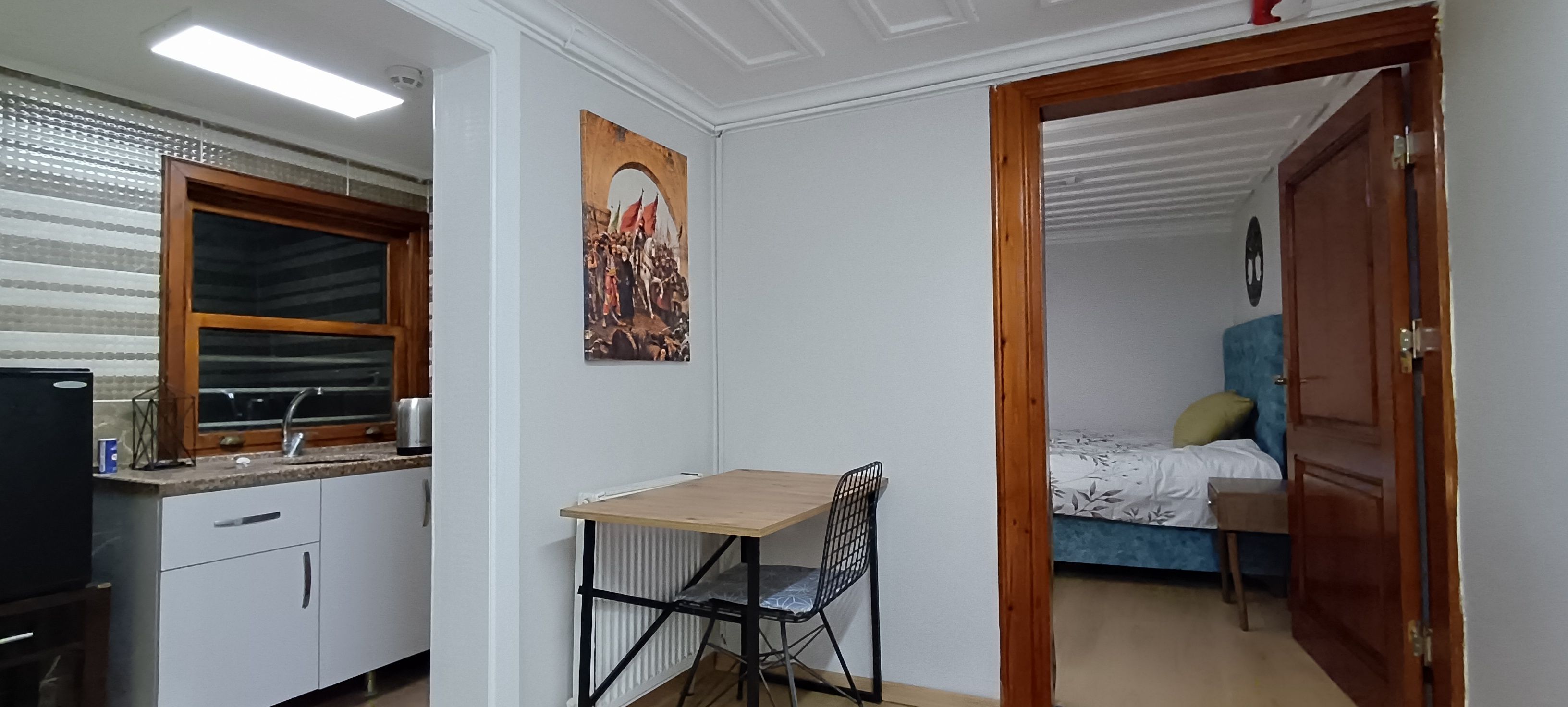 A compact room with a kitchenette, a bed, and a door leading to another room.
